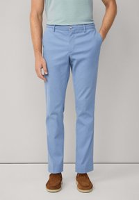 Light blue cotton trousers with a straight fit, front pockets, and a button closure. Worn with brown suede shoes. Minimalist design.