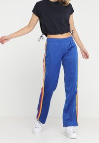 Modré sportovní kalhoty s rovný střih, vybavené bočními pruhy v červené, žluté a oranžové barvě. V kombinaci s černým zkráceným topem a bílými teniskami.