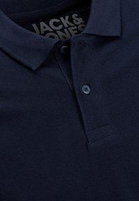 Polo shirt bleu marine avec un col, patte de boutonnage à deux boutons et un tissu texturé. L'étiquette visible à l'intérieur du col indique "JACK & JONES."