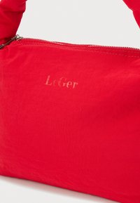Κόκκινη υφασμάτινη τσάντα με φερμουάρ και διακριτικό ανάγλυφο λογότυπο «LeGer» στο κέντρο της μπροστινής πλευράς, πάνω σε λευκό φόντο.