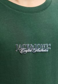 Grøn bomulds T-shirt med rund hals, ribbet halsudskæring og broderet "JACK & JONES Crafted Aesthetics" logo i hvid og sort.