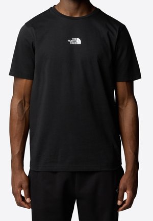 Homme portant un T-shirt noir à manches courtes avec un logo blanc "The North Face" sur la poitrine, devant un fond uni.