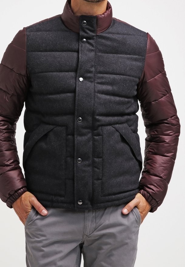 Vadderad jacka med en kropp av svart ullliknande material och bourgognefärgade kviltade ärmar. Den har en hög krage och framknäppning med två sidofickor.