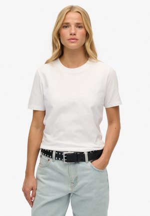T-shirt bianco in cotone con maniche corte, scollatura rotonda e logo in rilievo discreto, abbinata a jeans blu chiaro e una cintura nera con borchie.
