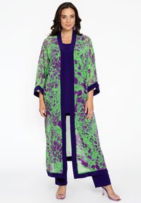 Lang, gennemsigtig kimono med grønne og lilla leopardmønstre, med en mørk lilla kant. Båret over et matchende outfit under.