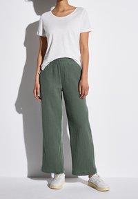 T-shirt bianco a maniche corte abbinato a pantaloni verde oliva a vestibilità ampia con texture sgualcita e sneaker bianchi. Design semplice, stile casual.