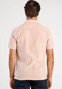 Koszula z krótkim rękawem w jasnoróżowym kolorze z teksturowanymi paskami i kołnierzykiem na guziki. Posiada boczne rozcięcia dla większego komfortu.