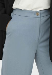 Pantalons cintrés bleu clair avec fermeture à bouton, poche frontale discrète et texture de tissu lisse. Assortis avec un haut noir superposé.