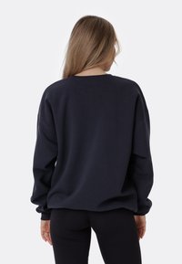 Felpa di un blu navy scuro con una vestibilità comoda, scollo rotondo e spalle cadenti. Tessuto morbido con maniche lunghe e polsini a costine.