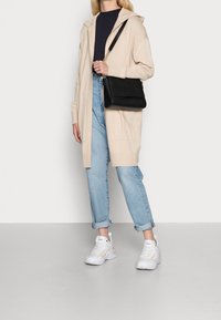 Beżowy długi kardigan, granatowa bluzka, jasnoniebieskie podwinięte jeansy, białe trampki z beżowymi akcentami. Czarna torba na ramię z fakturowanym wykończeniem.