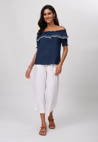 Top blu navy senza spalle con orlo arricciato, abbinato a pantaloni bianchi a gamba larga e sandali marroni. Tessuto leggero con sottile texture.