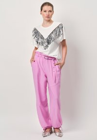 Witte T-shirt met een zilveren paillettenfranje detail bij de halslijn, gecombineerd met roze broeken met elastische taille en zakken.