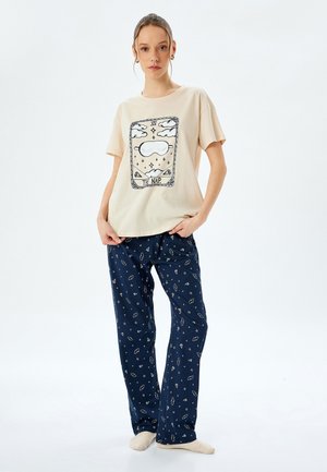 Beige katoenen t-shirt met "NAP" graphic, gecombineerd met marineblauwe pyjamabroek met een wit sterrenpatroon. Zachte, relaxte pasvorm, korte mouwen.