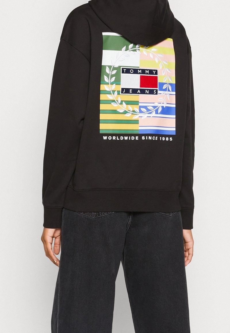 Hoodie noir avec un graphique coloré au dos portant le texte "TOMMY JEANS" et un design de laurier sur un patchwork de rayures et de couleurs.