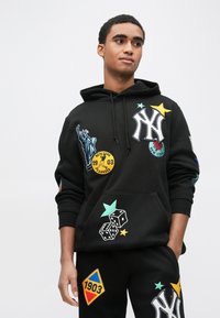 Czarna bluza z kapturem z naszywkami, w tym Statua Wolności i logo New York Yankees. Zawiera kolorowe wzory gwiazd i kości do gry.