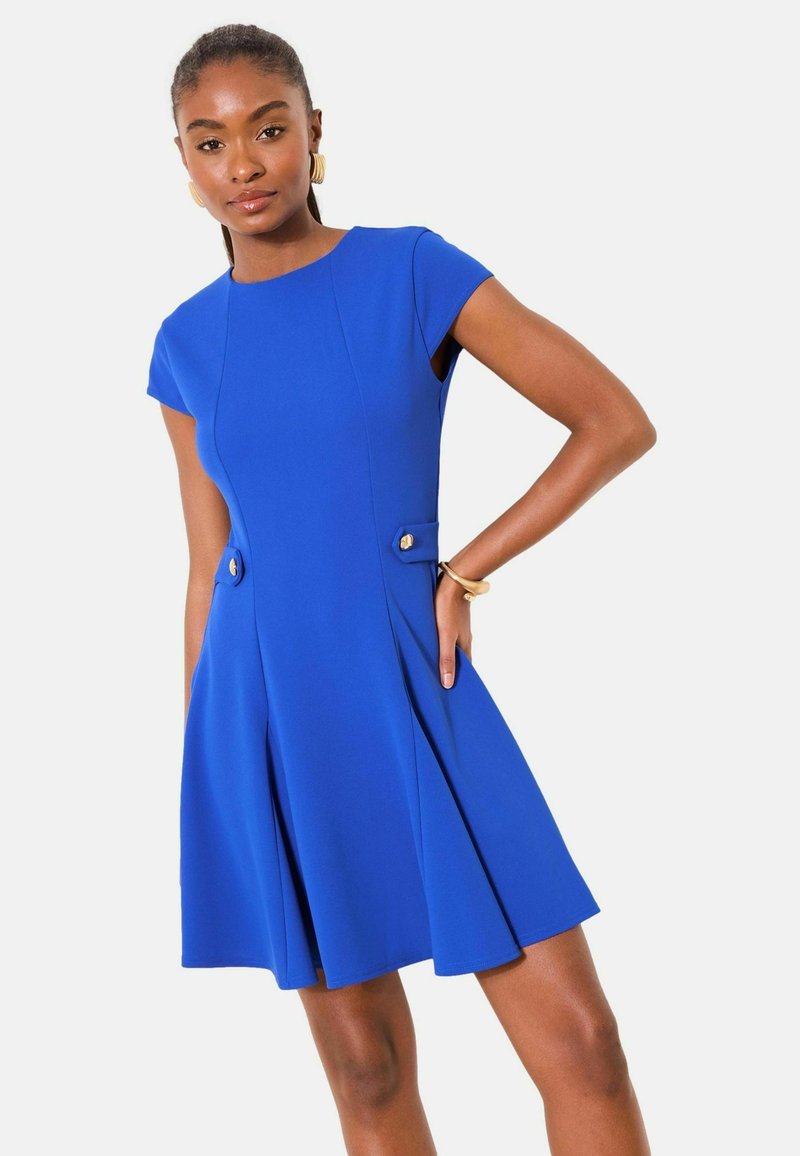 Sukienka o długości do kolan z krótkimi rękawkami w żywym niebieskim kolorze. Posiada fałdy z przodu oraz dwa ozdobne złote guziki na biodrach. Gładka faktura.
