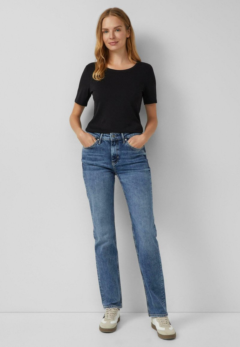 Schwarzes Kurzarm-T-Shirt kombiniert mit hellblauen geraden Jeans und beigen Sneakers. Das Outfit hat ein schlichtes, lässiges Design.