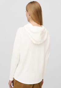 Sudadera ligera y blanca de manga larga con un ajuste relajado y una tela suave y texturizada, que presenta una capucha en la parte trasera y aberturas laterales en el dobladillo.