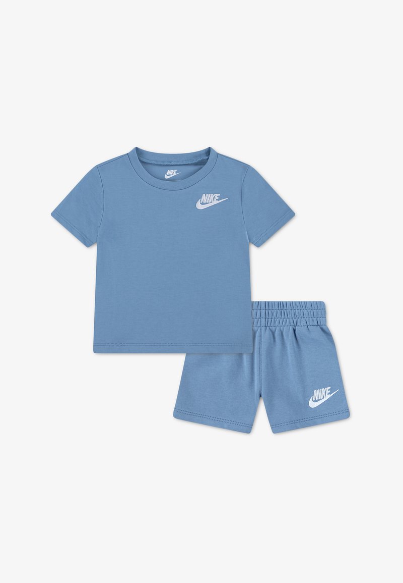 Μπλε μπλουζάκι Nike με κοντό μανίκι και σετ σορτς με ελαστική μέση, με λευκό λογότυπο Nike στο στήθος και στο αριστερό πόδι, τοποθετημένα επίπεδα σε λευκό φόντο.