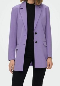 Lila bleiser, skreddersydd design med lange ermer, to svarte knapper og frontlommer. Brukt over en svart topp med svarte bukser.