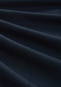 Tmavě modrá tkanina s texturovaným povrchem, vykazující více úhlových záhybů a hladký, rovnoměrný vzor tkaní.