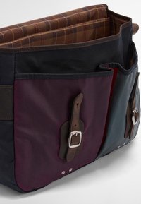 Saco messenger de tela em azul escuro, bordeaux e verde. Apresenta detalhes em couro e ferragens prateadas. O interior tem forro xadrez.