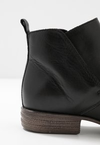 Bottine en cuir noir avec un bout arrondi, une finition texturée et un petit talon empilé. Comprend une languette pour un enfilage facile.