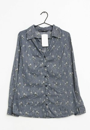 Blau-weiß gestreiftes, langärmliges Hemd mit Knopfleiste und kleinen weißen Blumenmustern, hängend an einem schwarzen Kleiderbügel, Vorderansicht mit Etikett.