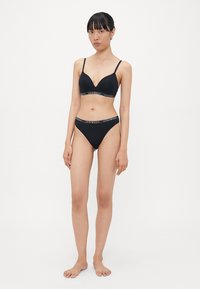 Zwart lingerieset bestaande uit een plunge beha met verstelbare bandjes en bijpassende low-rise slip, beide met een dunne band die is geaccentueerd met een logo.