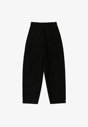 Czarne, wysokie, taperowane spodnie z pętelkami na pasek i dwiema dużymi przednimi kieszeniami, leżące na białym tle.