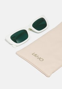 Occhiali da sole oversize bianchi con lenti verdi accanto a un morbido astuccio beige chiaro impresso con "LIU JO" in oro. Forma piatta e rettangolare, design moderno.