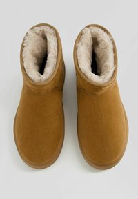 Bruna mockaskinn ankelstövlar med mjukt fuskpälsfoder, rund tå och gummisula. Ovandelen har sömlösa sömmar längs sidorna.