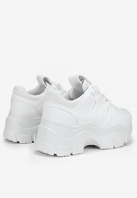 Zapatillas deportivas blancas de plataforma con parte superior sintética texturizada, puntera redondeada, suela gruesa y diseño con cordones. Contorno notable a lo largo de los lados.