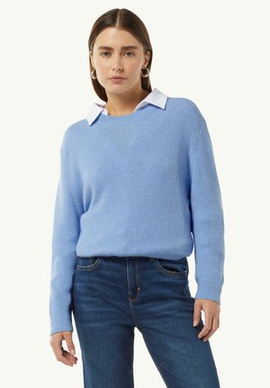 Helles blauer Rippenpullover mit langen Ärmeln, einem runden Ausschnitt und einem weißen Hemd darunter, kombiniert mit dunklen Jeans.