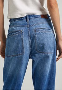 Light blue denim jeans with a relaxed fit, featuring two back pockets and orange stitching along the seams and pockets.