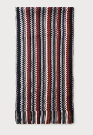 Écharpe tricotée avec des rayures zigzag verticales en noir, gris, blanc et couleur rouille, avec des franges aux deux extrémités.