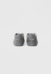 Een paar grijze Vans lage sneakers gezien van achteren op een plain witte achtergrond.