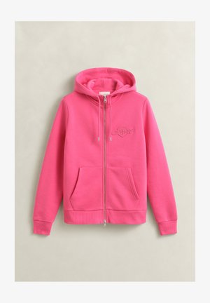 Sweat à capuche zippé rose vif avec poches avant, capuche réglable par cordon et logo brodé discret sur la poitrine, présenté sur un fond neutre.
