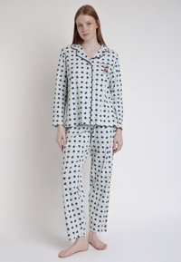 Conjunto de pijama de algodón con un fondo gris claro y pequeños patrones de corazones en azul marino, contrastado con ribetes oscuros y un bordado descriptivo.