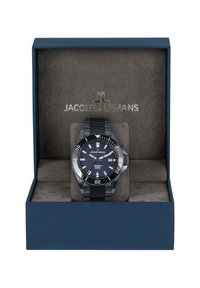 Jacques Lemans ur i en marineblå kasse; sort metalrem, rund blå urskive med sølvdetaljer, datovisning og roterende bezel.