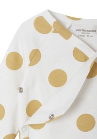 White cotton romper featuring large golden polka dots, with snap closures and contrasting stitching along the wrap design.