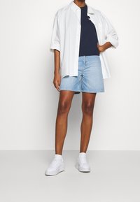 Vit oversized skjorta med knappar, marinblå t-shirt, ljusblå denimshorts och vita sneakers. Funktioner inkluderar uppvikta ärmar och avslappnad passform.