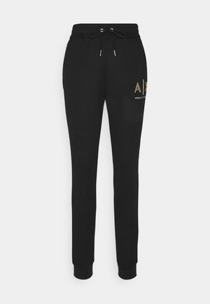 Černé tepláky s páskem na stažení v pase, zdobené zlatým logem a elastickými manžetami u kotníků. Vyrobené z měkké látky.