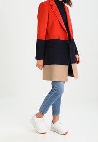 Röd, marinblå och beige färgblockerad kappa i ullblandning. Har en enkel knappstängning, notched lapels och två framfickor.