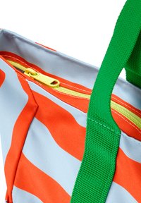 Primo piano di una borsa con strisce arancioni e azzurro chiaro, una cerniera gialla e un manico in tessuto verde.