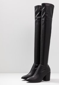 Zwarte over-de-knie laarzen van glad faux leer met een puntige neus en chunkier blokhak, voorzien van strakke naden en een getailleerd ontwerp.