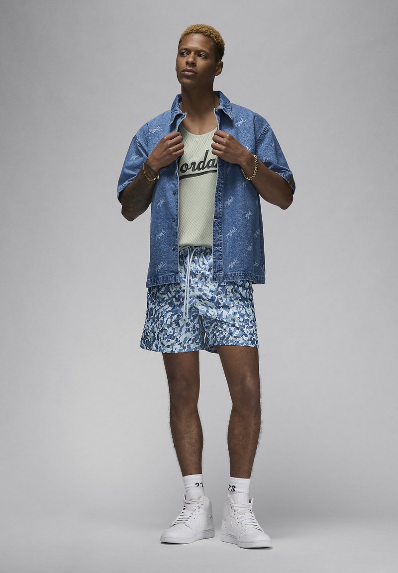 Chemise en jean à manches courtes avec motif brodé, débardeur en mesh vert clair avec logo, et shorts camouflage bleu. Baskets montantes blanches.