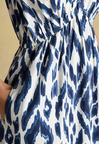 Zila un baltā dzīvnieku raksta kleita ar elastīgu vidukli, savelkamu detaļu un kabatām. Audumam ir gluda tekstūra.