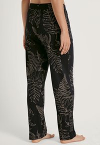Zwarte pyjamabroek met een botanisch varenpatroon in beige, voorzien van een elastische tailleband en een relaxed fit. Zachte textuur van de stof is zichtbaar.