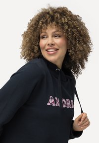 Námořnická mikina s růžovým potiskem "AMORE". Má kapuci se šňůrkou, jemnou texturu a volný střih. Jednoduchý, ležérní design.